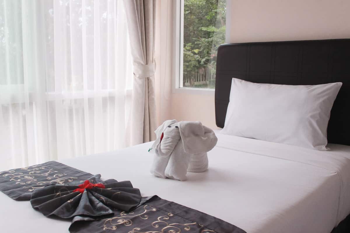A neatly made bed with a white pillow and a plush toy, a black and gold throw pillow, and sheer curtains.