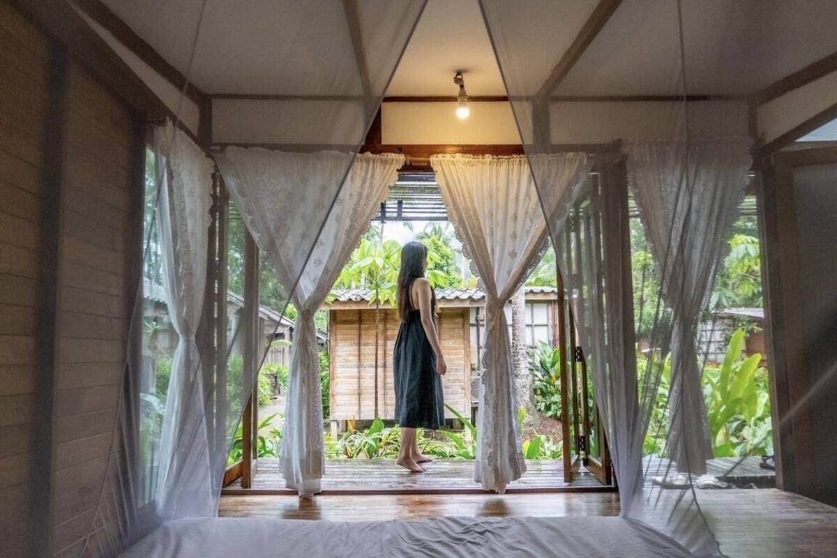 Quarto com cama, cortinas brancas e vista para um jardim.