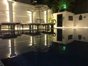 A reflective pool with tables and chairs, surrounded by walls with small windows and potted plants. - Champey Villa (Siem Reap)