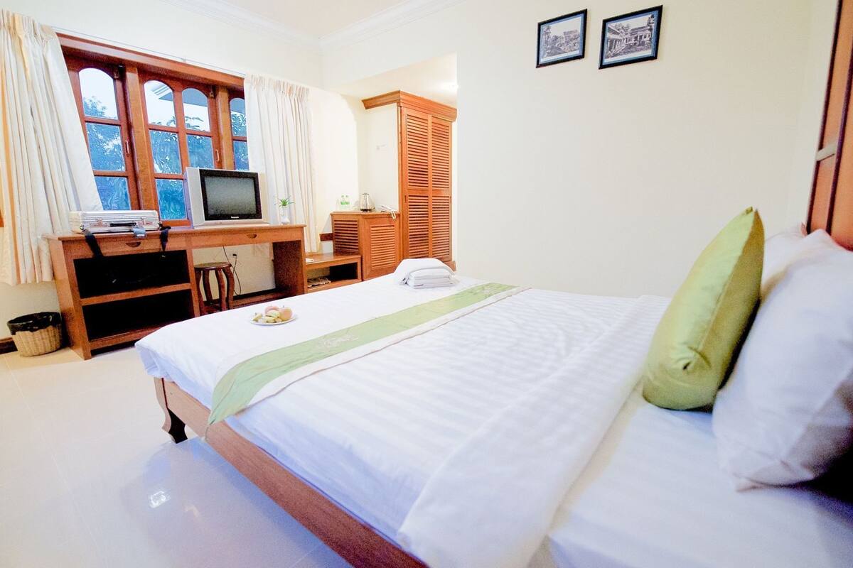 Ein Hotelzimmer mit einem Bett, einem Schreibtisch mit Computer, einem Fernseher und einem Fenster mit Vorhängen.