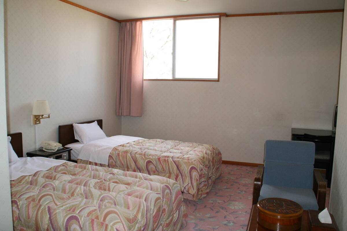 A hotel room with two beds, a desk, a chair, and a television.