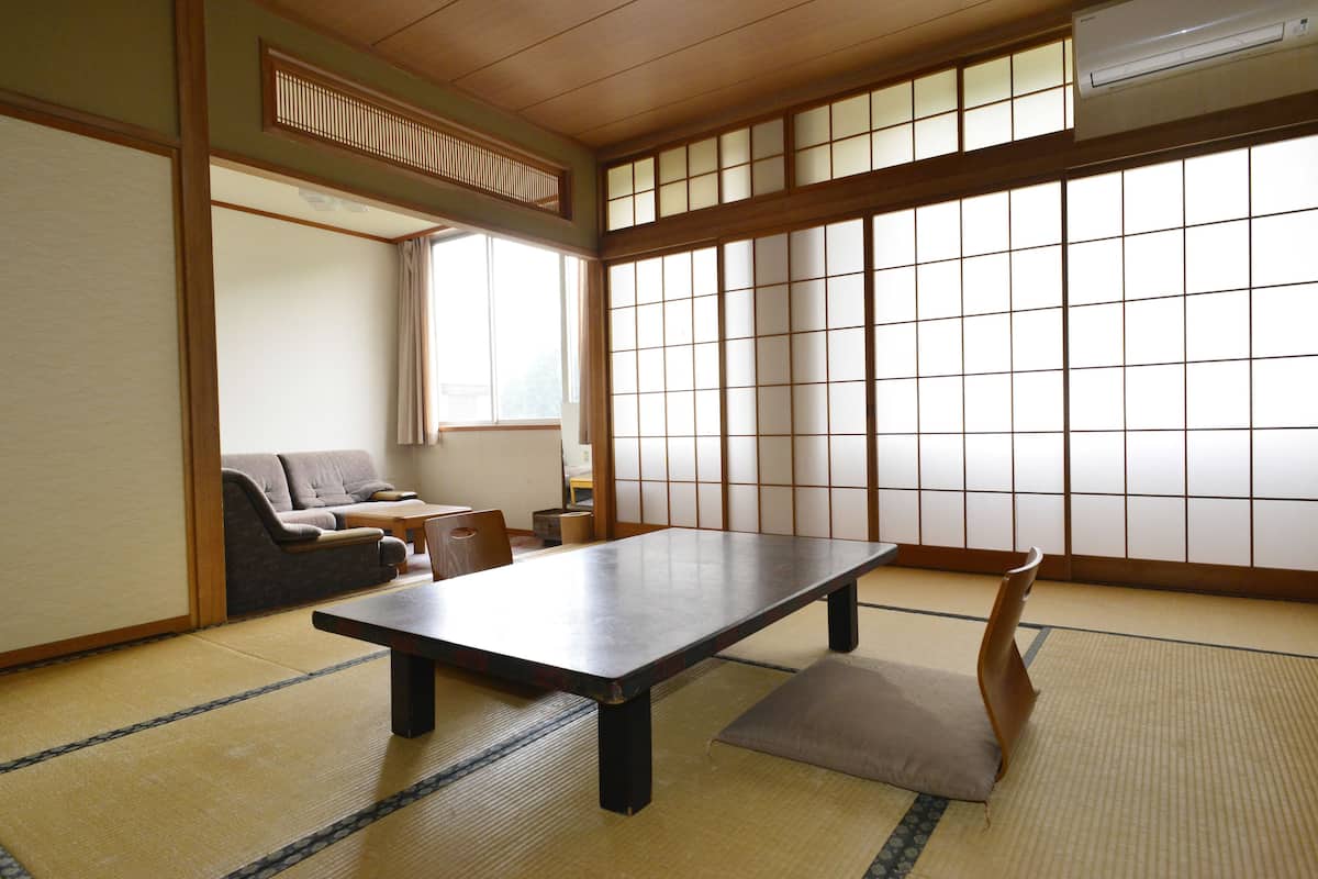 A traditional Japanese room with tatami flooring, a low table, a cushioned bench, and sliding shoji doors.
