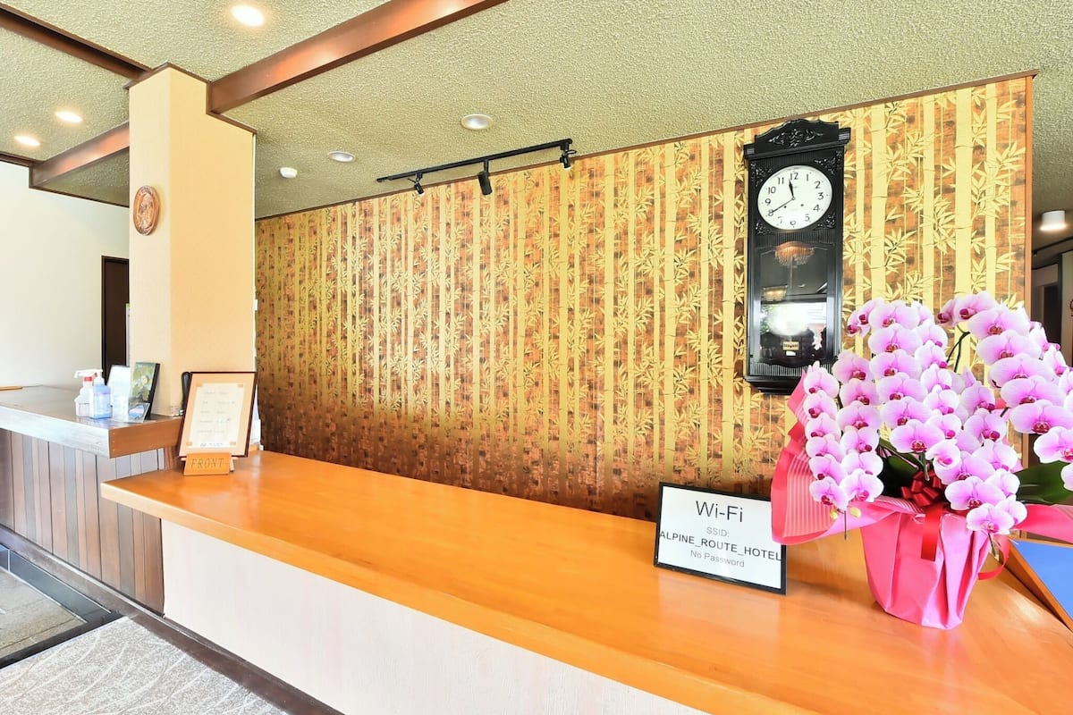 A hotel reception desk with a clock, a sign indicating Wi-Fi availability, and a floral arrangement.