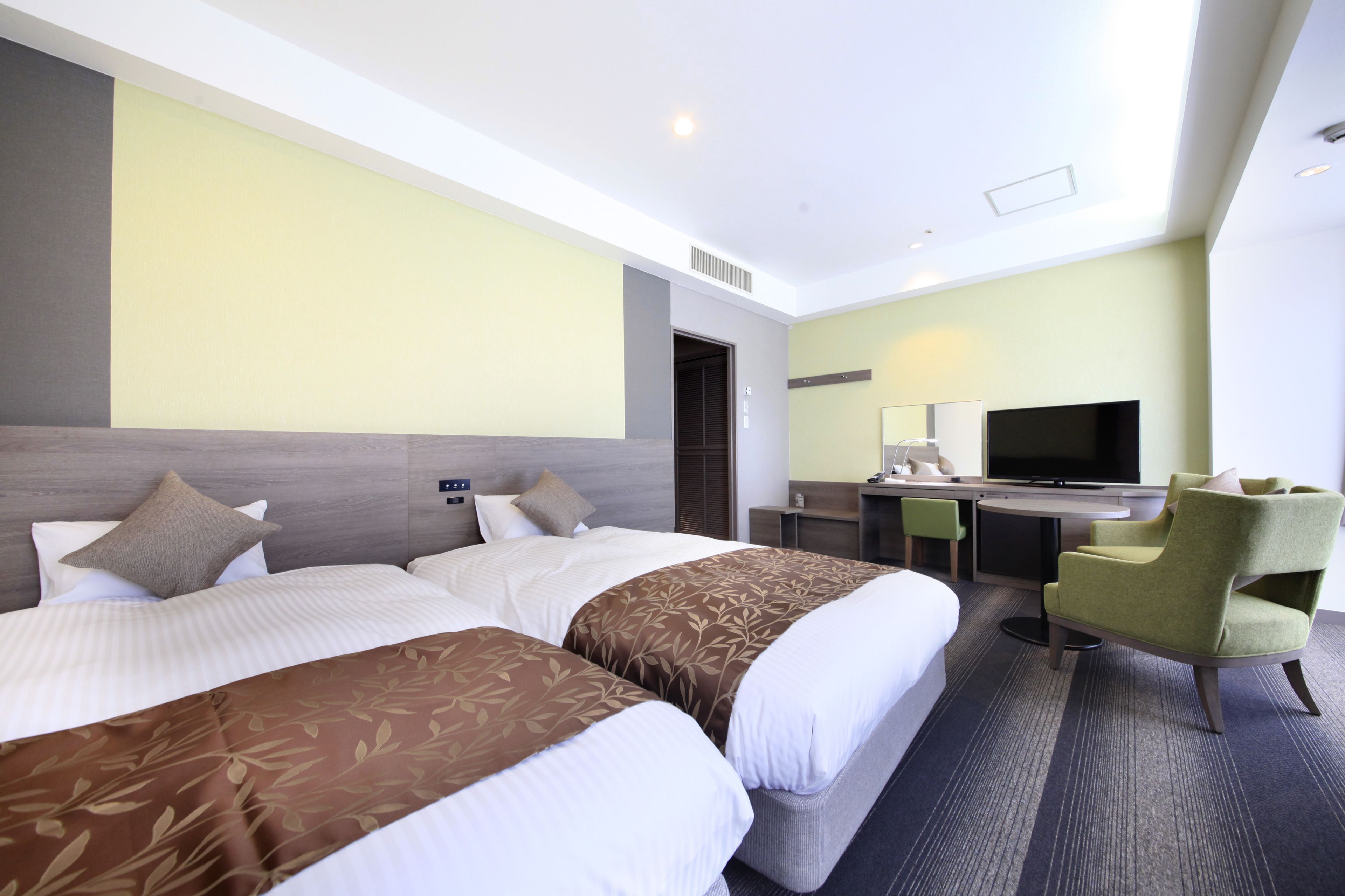 A hotel room with two beds, a desk, a chair, and a television.