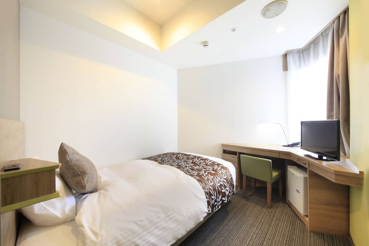 A hotel room with a bed, a desk with a computer, a chair, and a television.