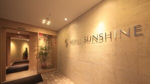 Entrada de hotel con suelo de baldosas, una escalera y una pared con el nombre del hotel.