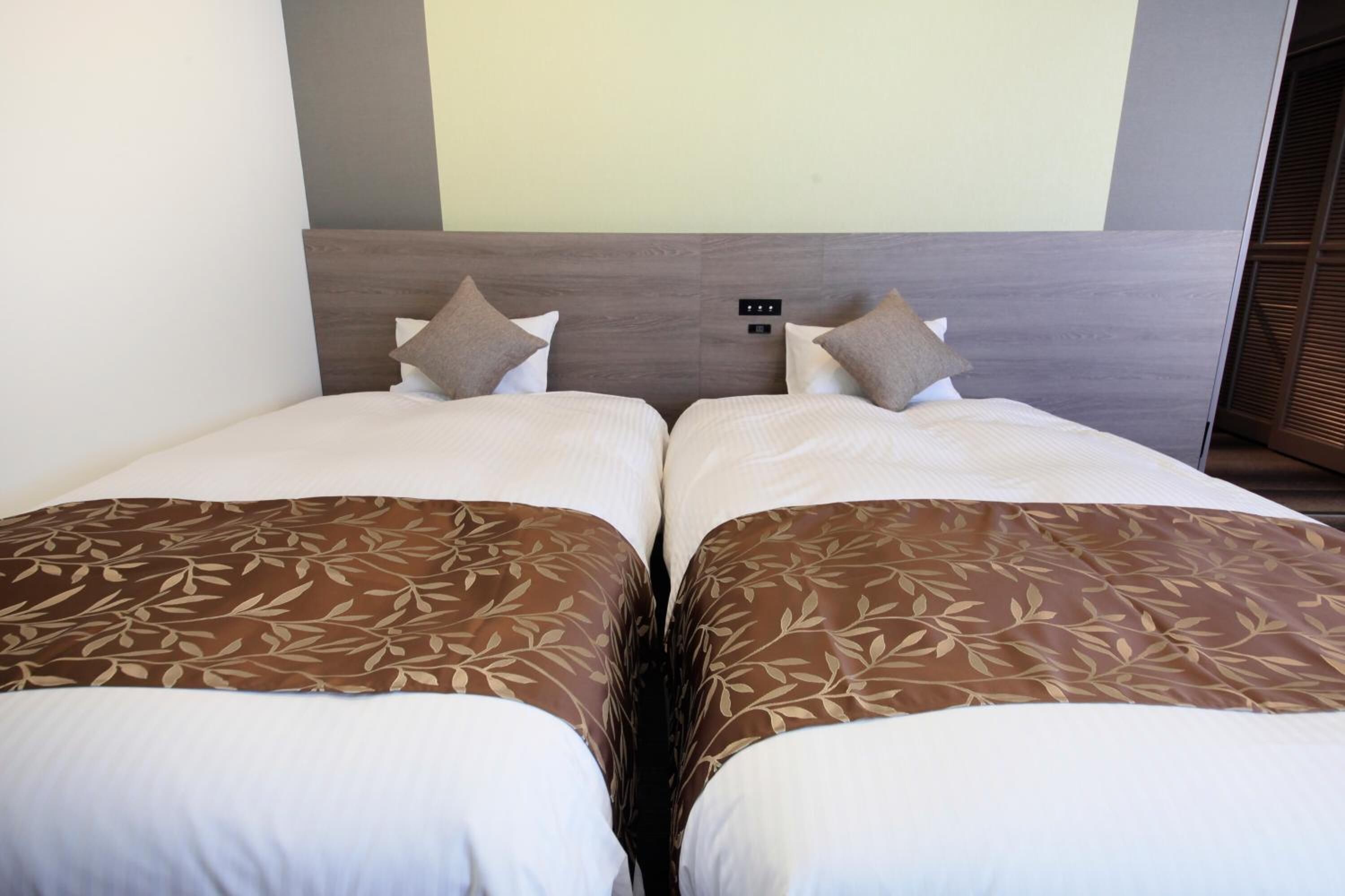 A double bed with a wooden headboard, two pillows, and a leaf-patterned bedspread.