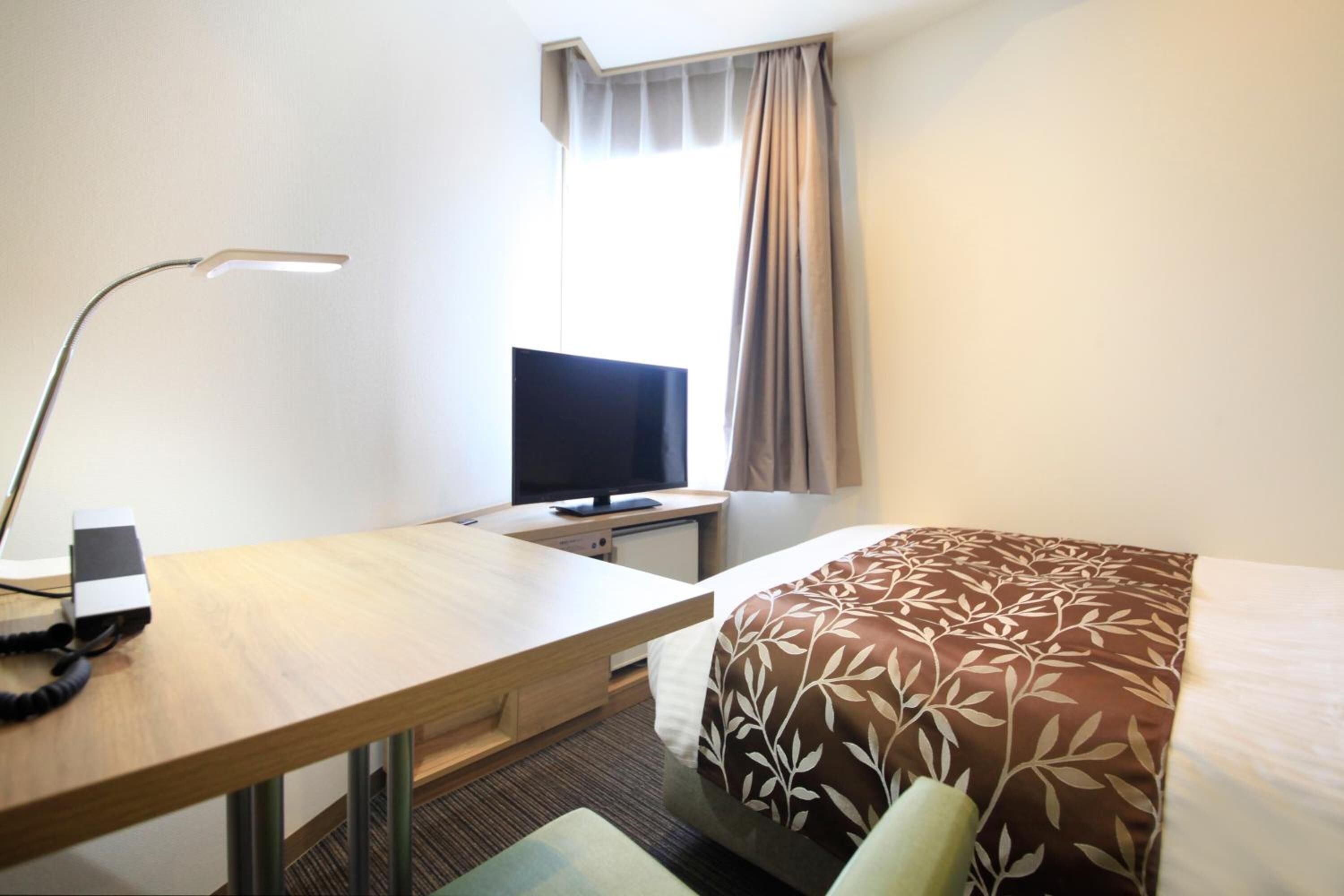 A hotel room with a bed, a desk with a computer, a lamp, and a television.