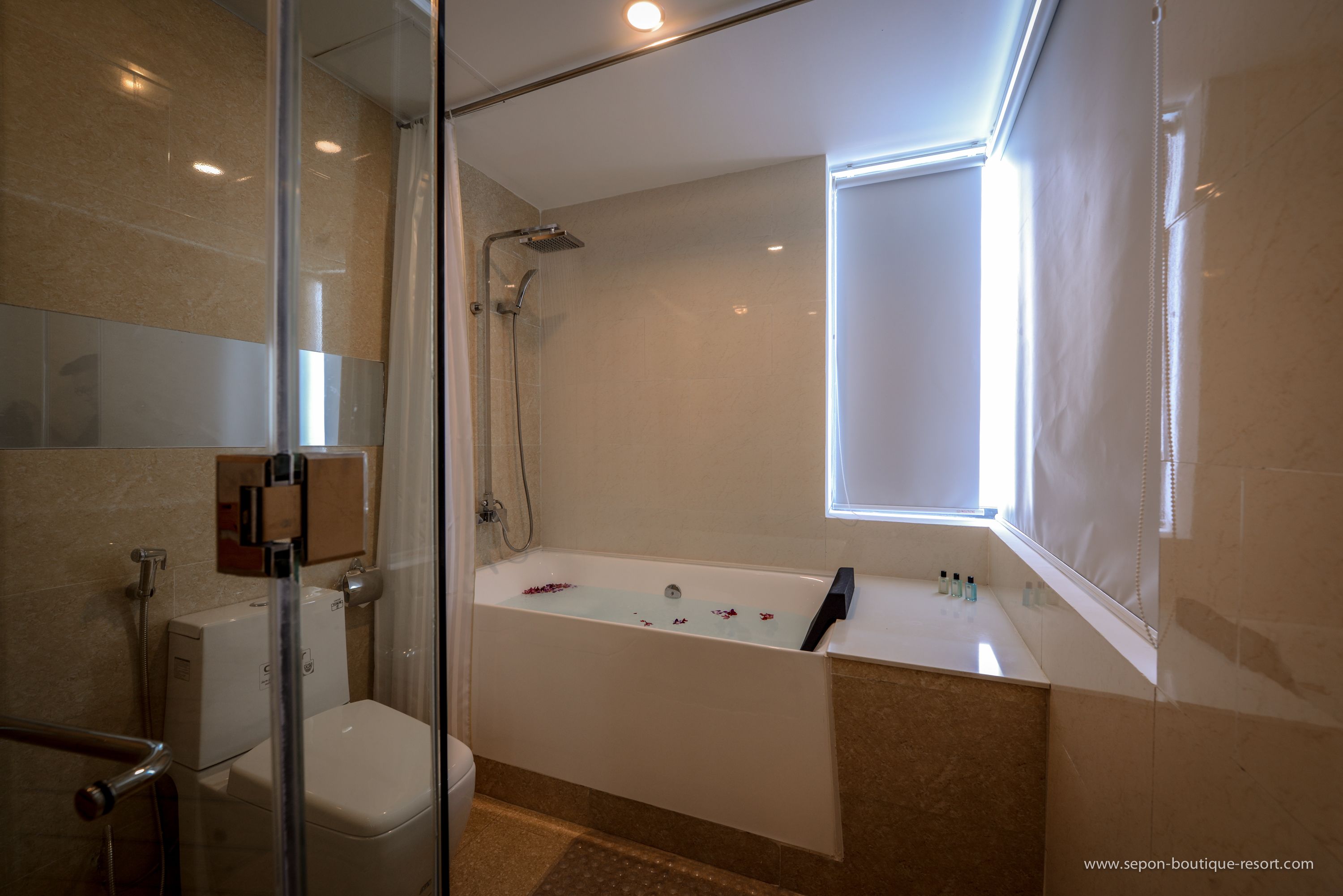 A modern bathroom with a glass shower enclosure, a bathtub with rose petals, and a window providing natural light.