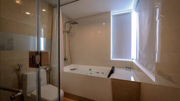 A modern bathroom with a glass shower enclosure, a bathtub with rose petals, and a window providing natural light.