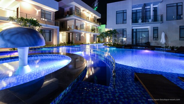 Ein modernes Hotel mit Schwimmbad, Springbrunnen und gut beleuchteter Fassade.