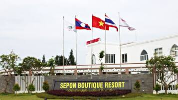 Um edifício com bandeiras, uma placa com a inscrição "SEPON BOUTIQUE RESORT" e um jardim bem cuidado.