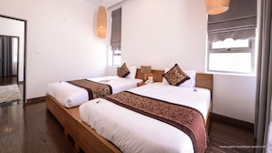 Ein Hotelzimmer mit zwei Betten, Holzboden, einem fensterbepflanzten Fenster und einer Pendelleuchte.