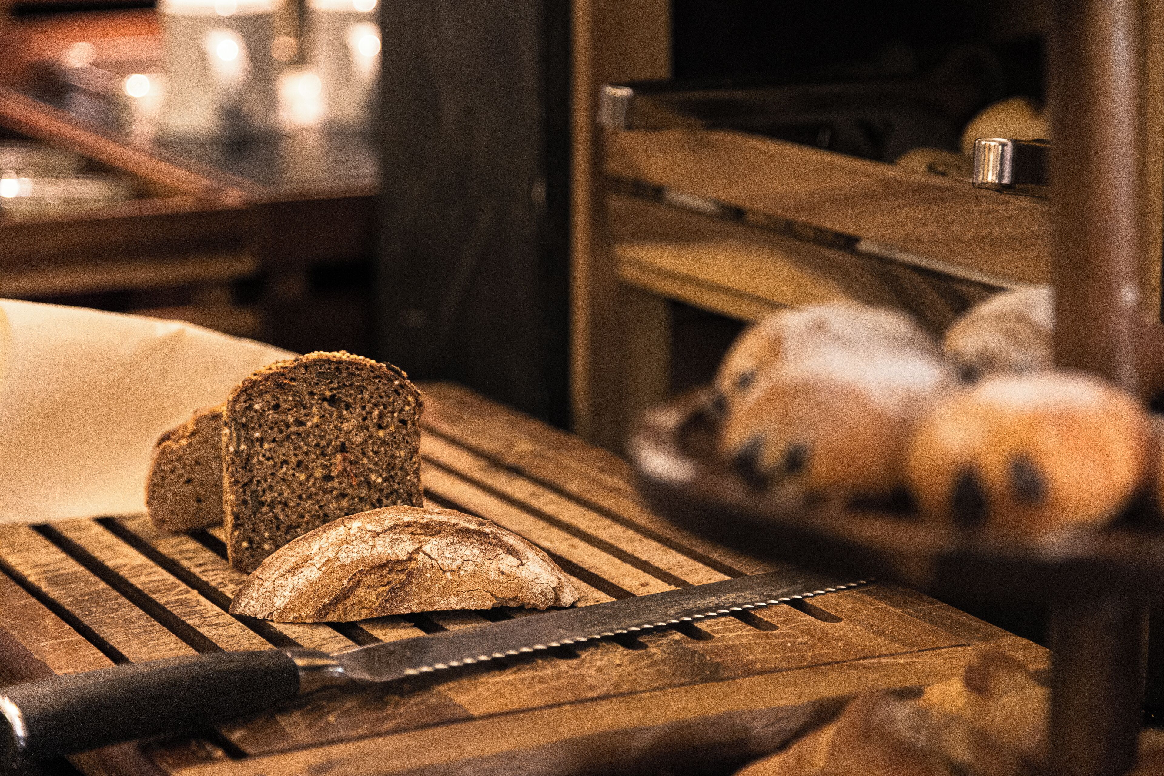 Une table en bois sur laquelle se trouvent un pain, un couteau et un panier de viennoiseries.