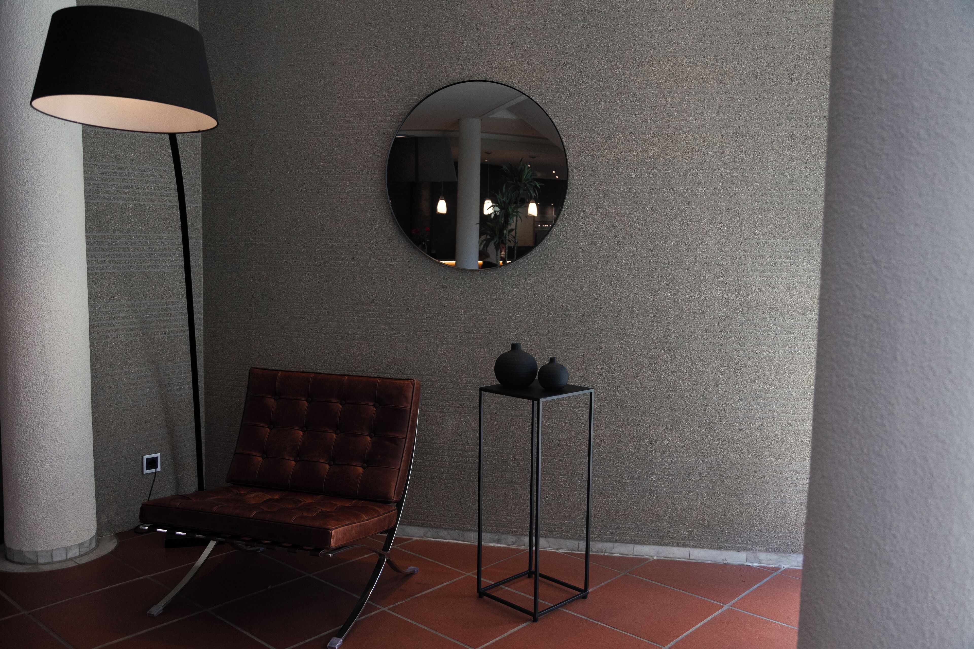 Una habitación moderna con un sillón de cuero marrón, un espejo redondo en la pared y una lámpara de pie alta.