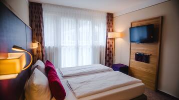 Una habitación de hotel con cama, televisor, escritorio y ventana con cortinas.