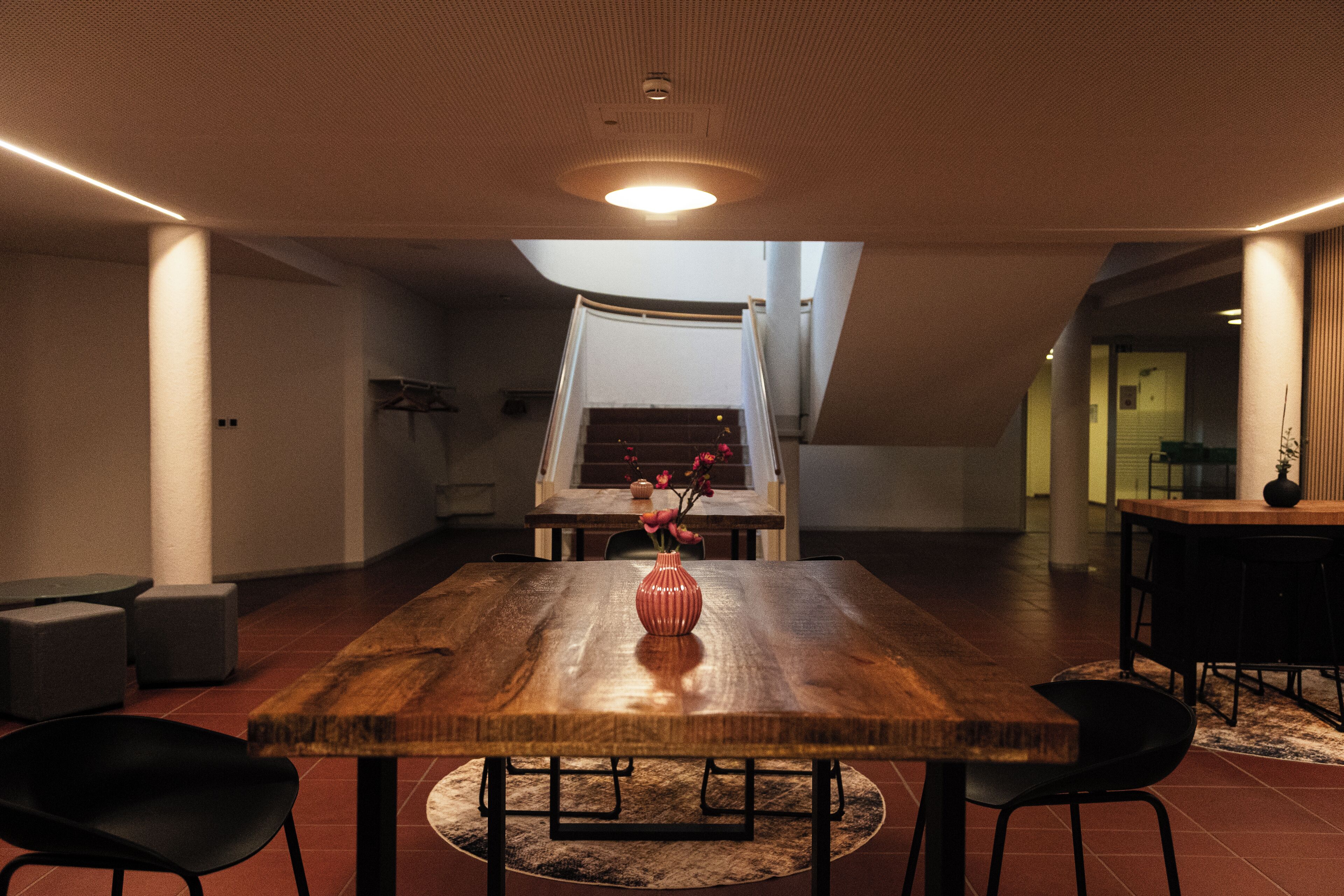 Ein geräumiges Zimmer mit einem großen Holztisch, einer Vase mit Blumen und Blick auf eine Treppe.
