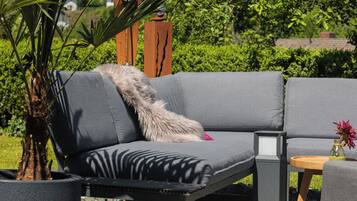 A gray sofa with a fur throw, a small wooden table with a vase, and a potted plant.