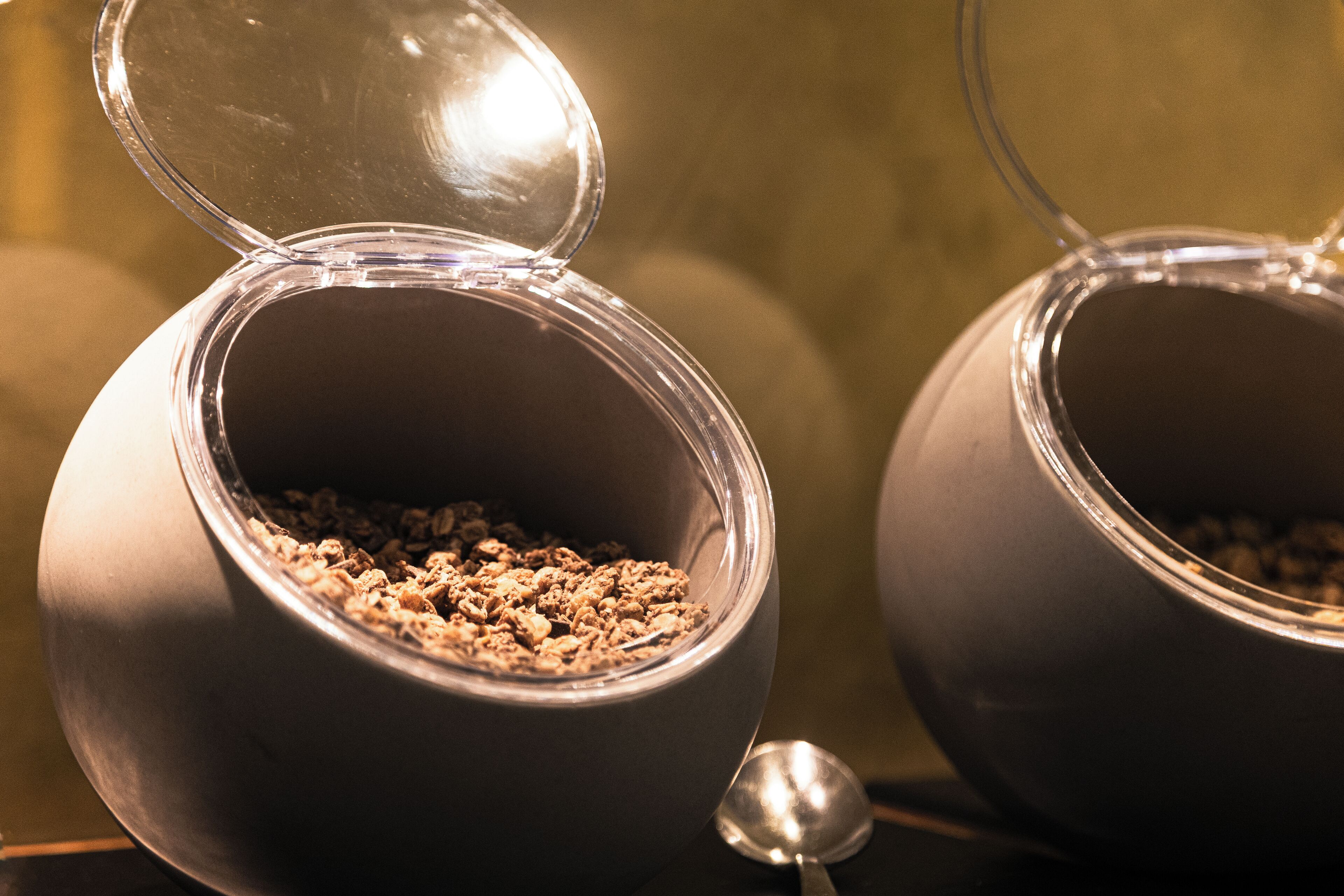 Dos recipientes esféricos con tapas, llenos de granola, y una cuchara a su lado.
