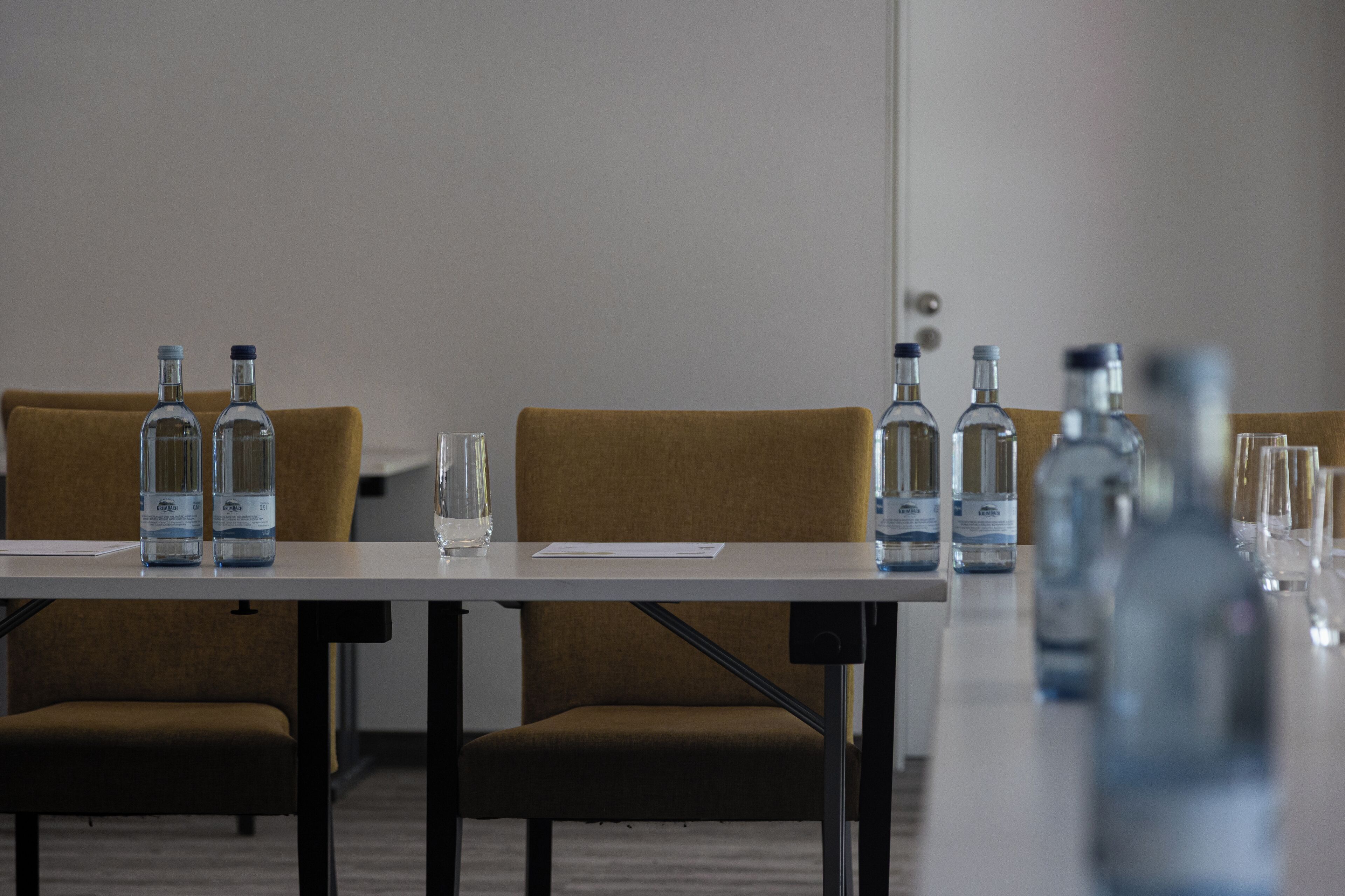 A conference table with water bottles and glasses, two brown chairs, and a door in the background.