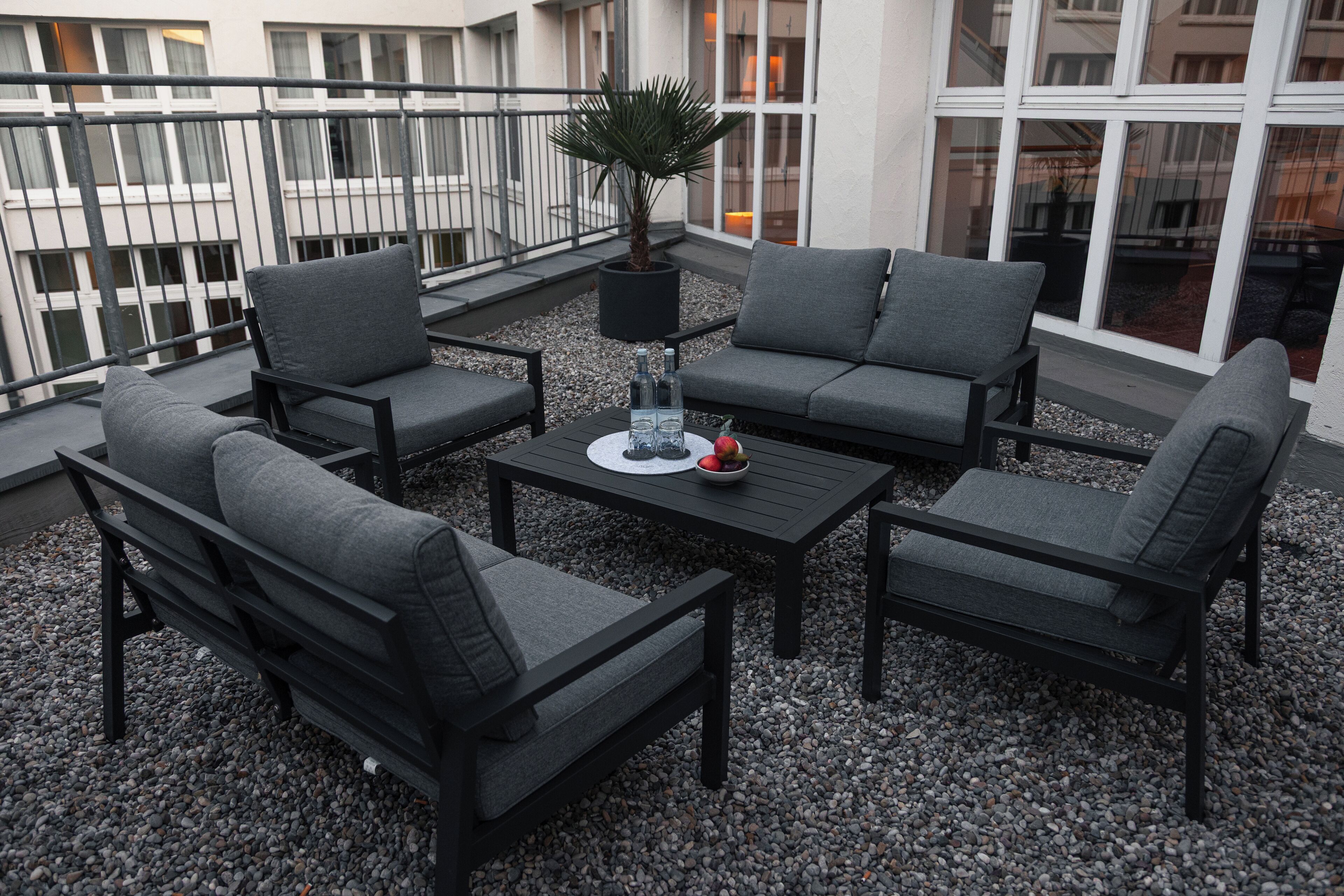 A balcony with outdoor seating, including two sofas and a bench, surrounded by gravel.