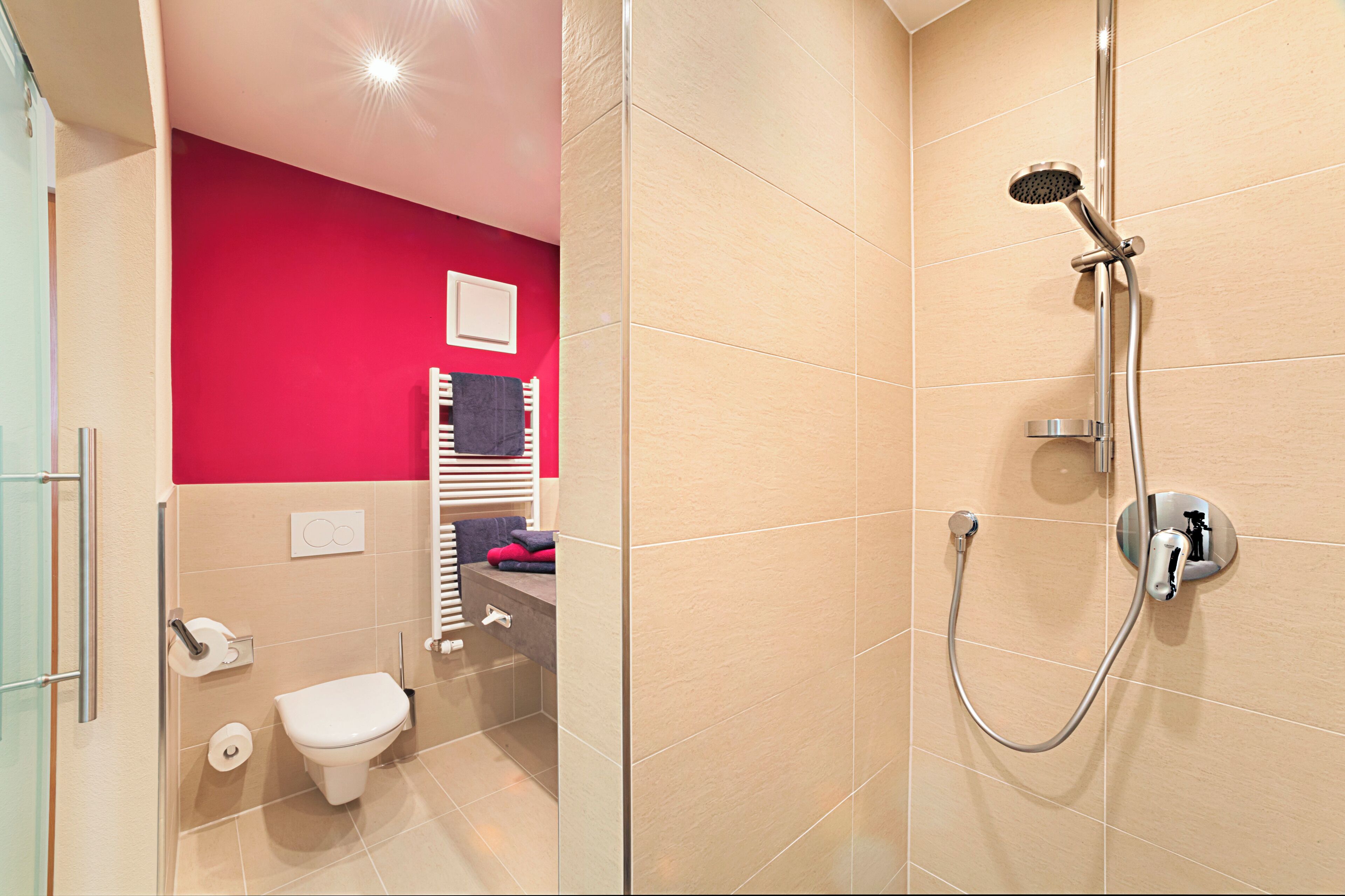 Une salle de bain moderne avec douche, toilettes et un mur d’accent de couleur rouge.
