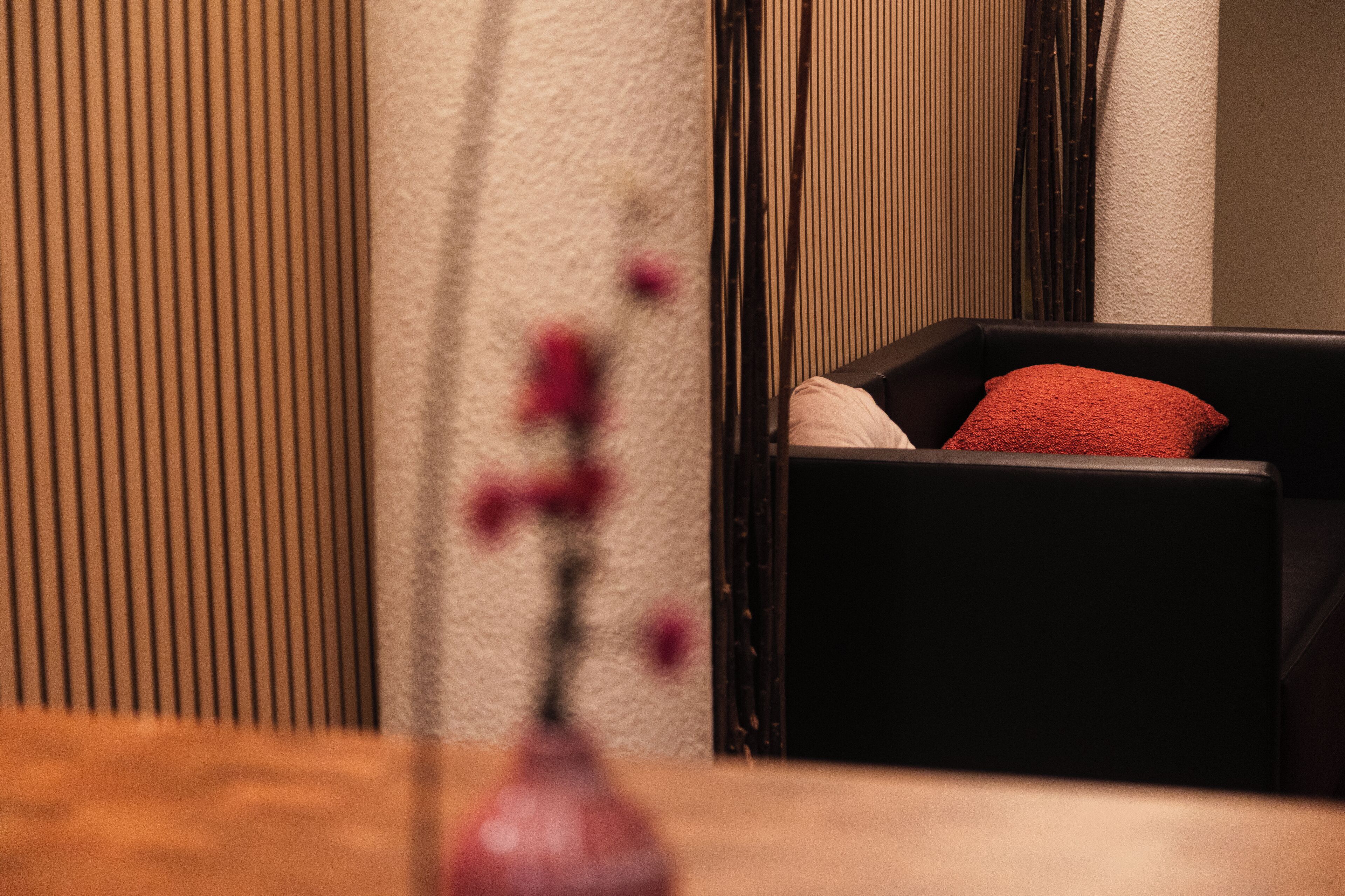 A modern room with a wooden table, a black chair with a red pillow, and a vase with flowers.