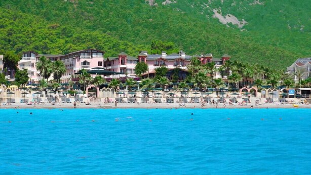 Un hotel frente a la playa con varias construcciones, una playa de arena y un mar azul cristalino.