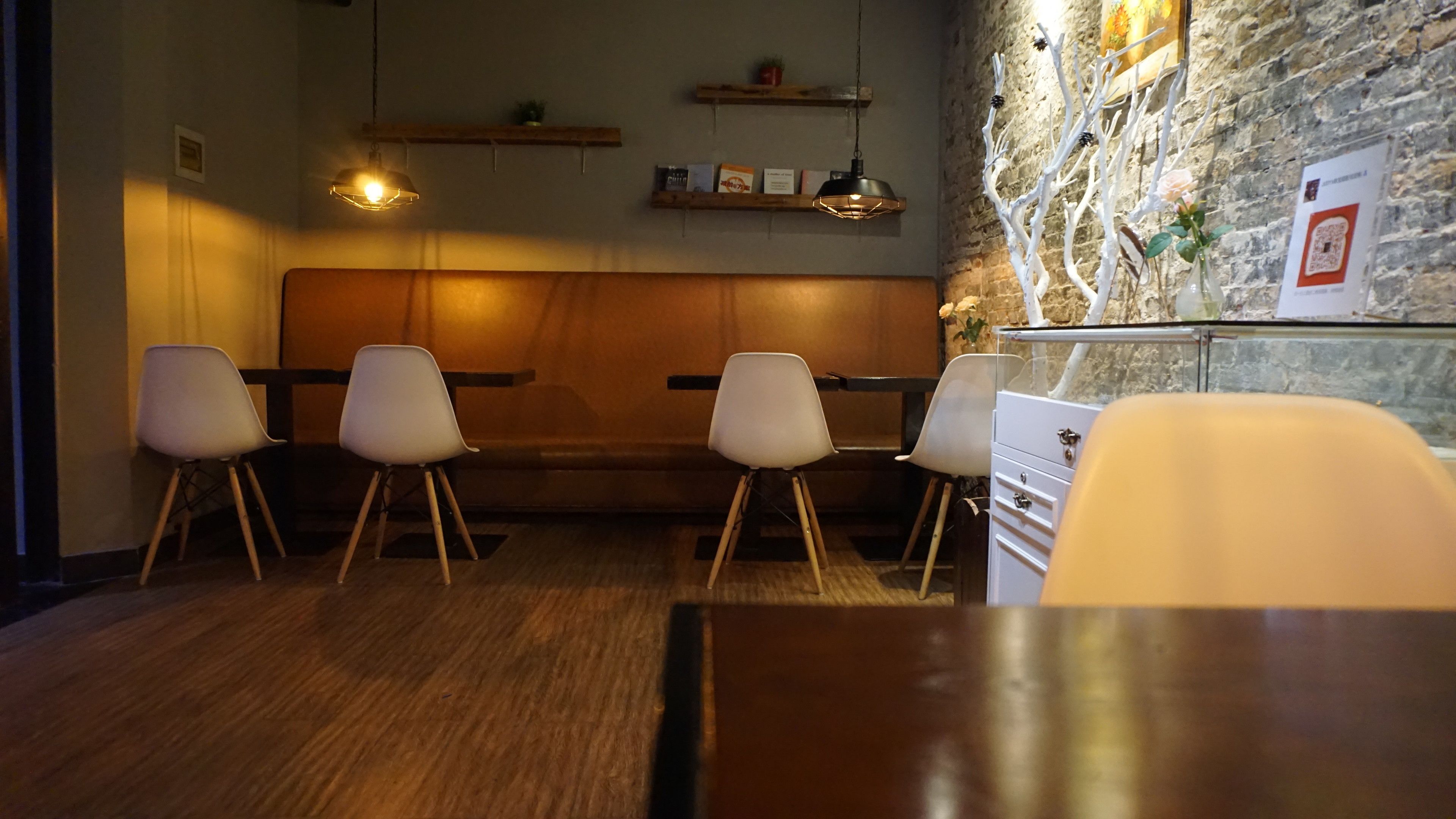 A restaurant interior with wooden tables and chairs, a stone wall, and hanging lights.