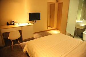 Una camera d'albergo con un letto, una scrivania con un computer, una sedia, una televisione e un bagno con un lavandino e uno specchio.
