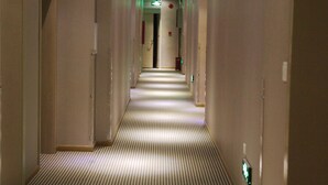 Et hotel med korridor, et stribet tæppe, indbygget lys og en dør for enden.