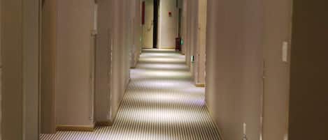 Un pasillo de hotel con alfombra a rayas, iluminación empotrada y una puerta al final.