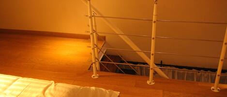 A room with a wooden floor, a metal rack, and a staircase in the background.