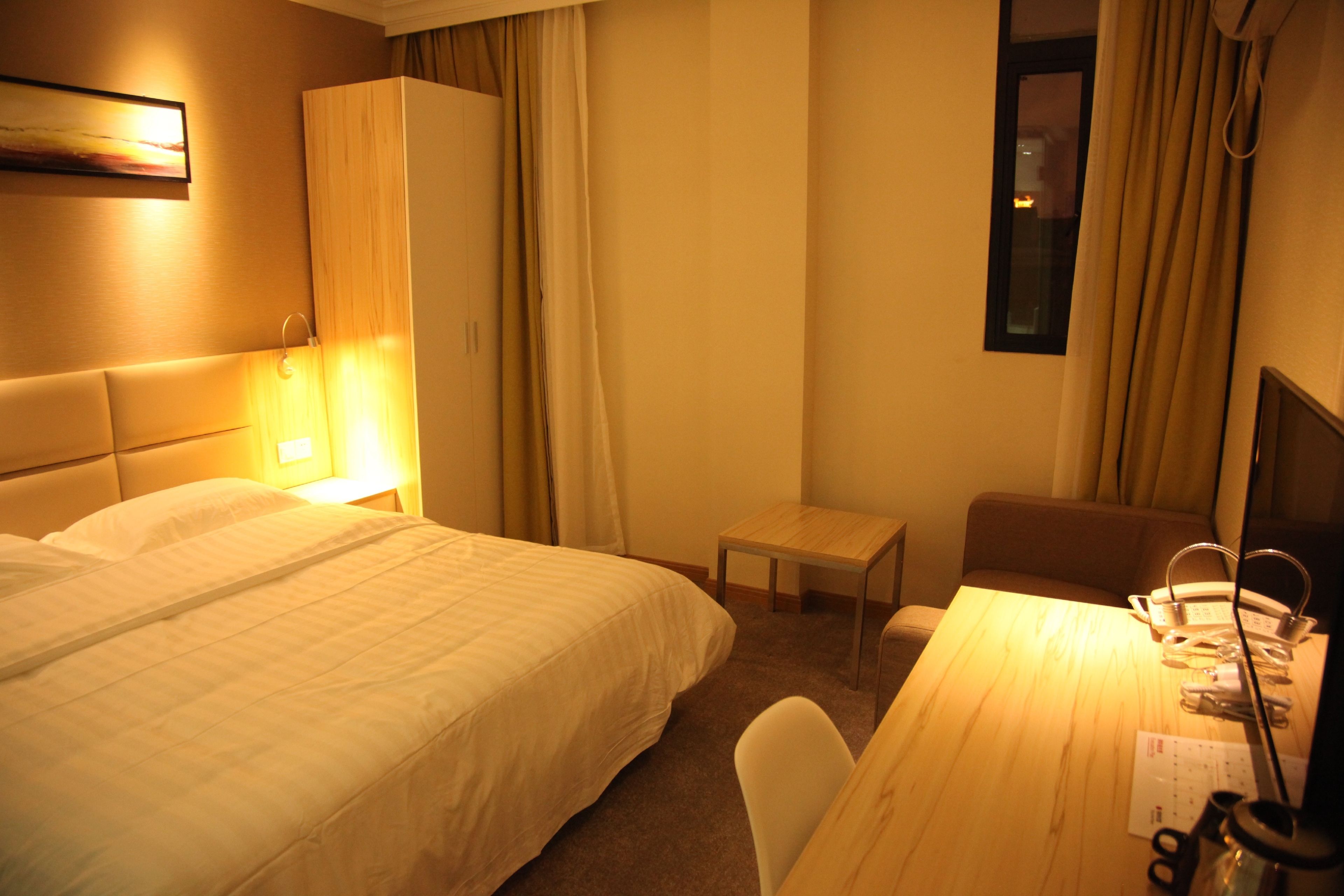 A hotel room with a bed, a desk with a chair, a small table, and a wardrobe.