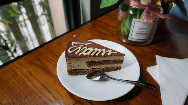 Une part de gâteau à plusieurs couches, servie sur une assiette blanche avec une cuillère, est posée sur une table en bois.