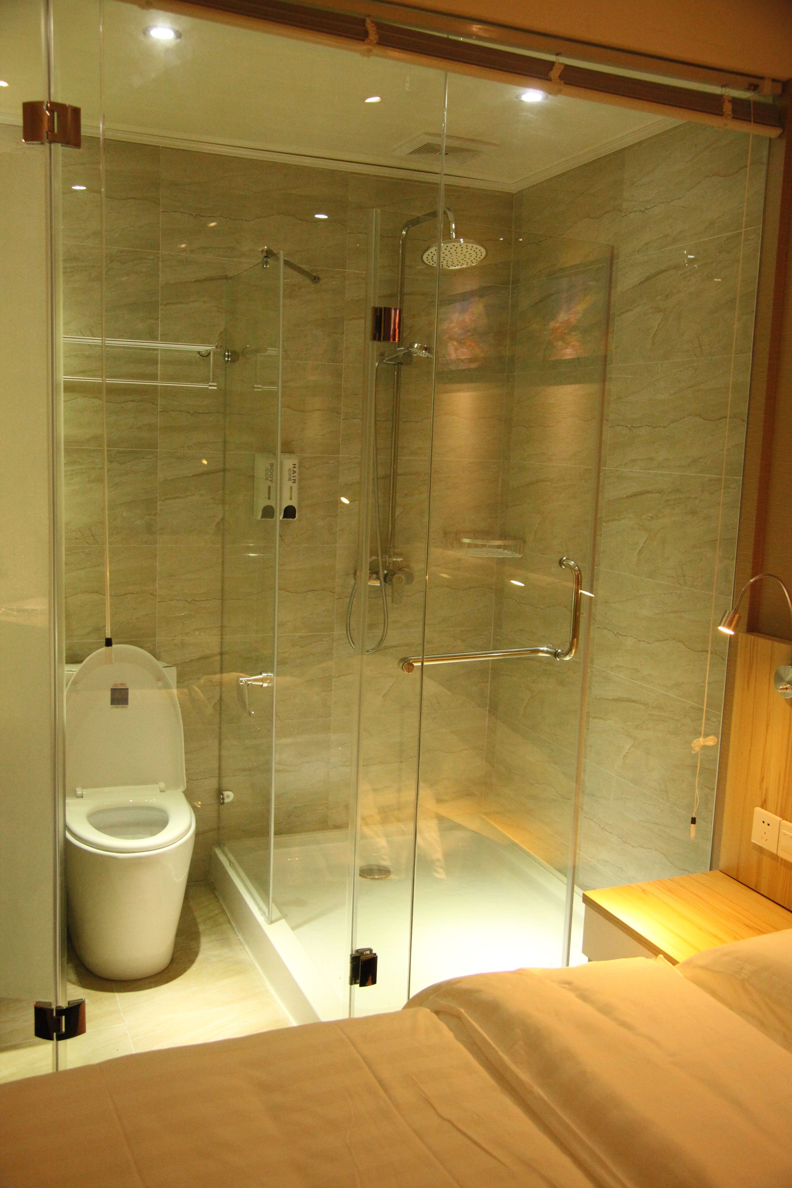 A modern bathroom with a glass-enclosed shower, a toilet, and a wooden bench.