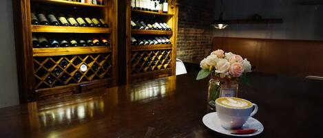 A bar area with wooden shelves of wine bottles, a vase with flowers, and a cup of coffee on a saucer.
