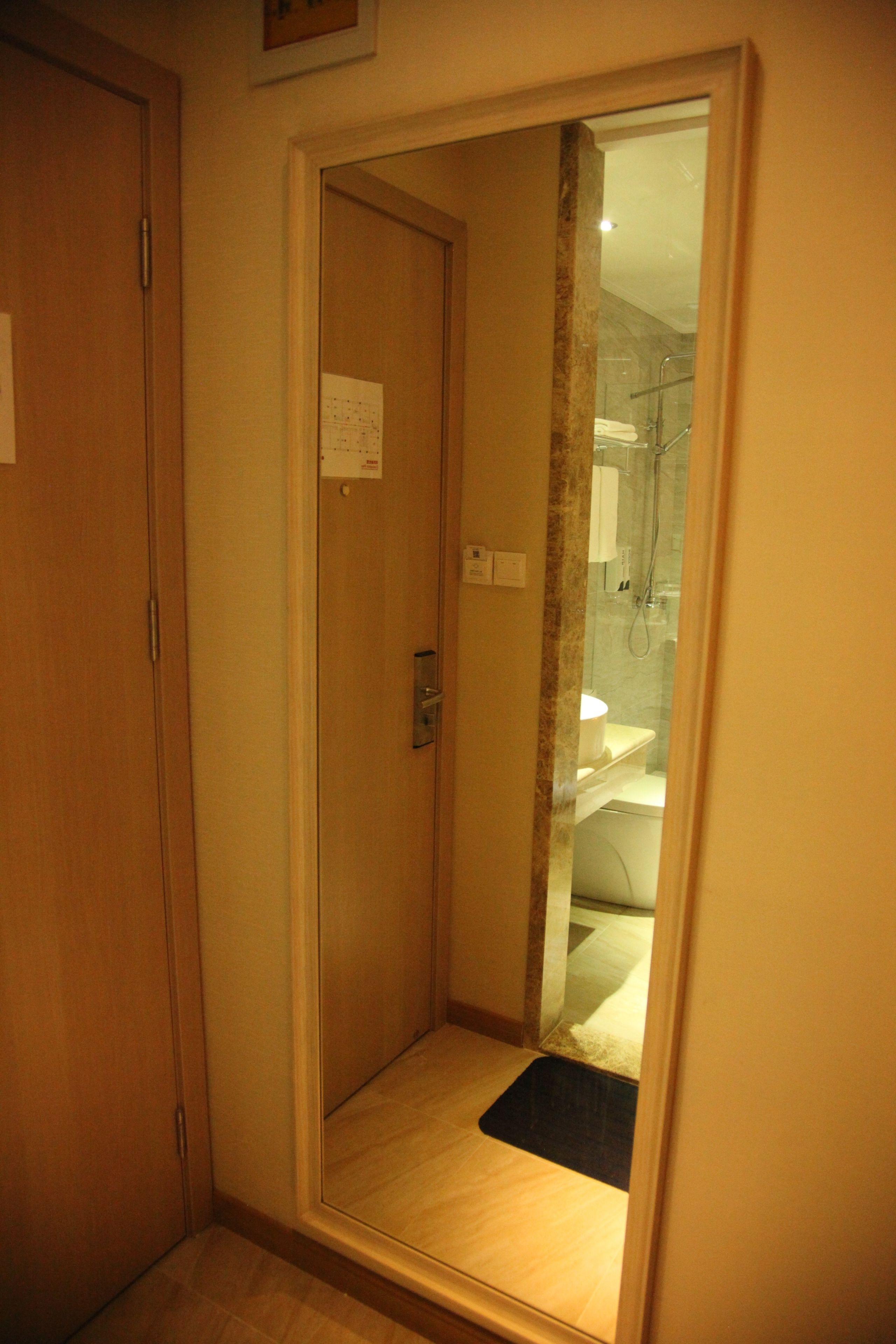 A narrow hallway leading to a bathroom with a shower, a toilet, and a small rug on the floor.