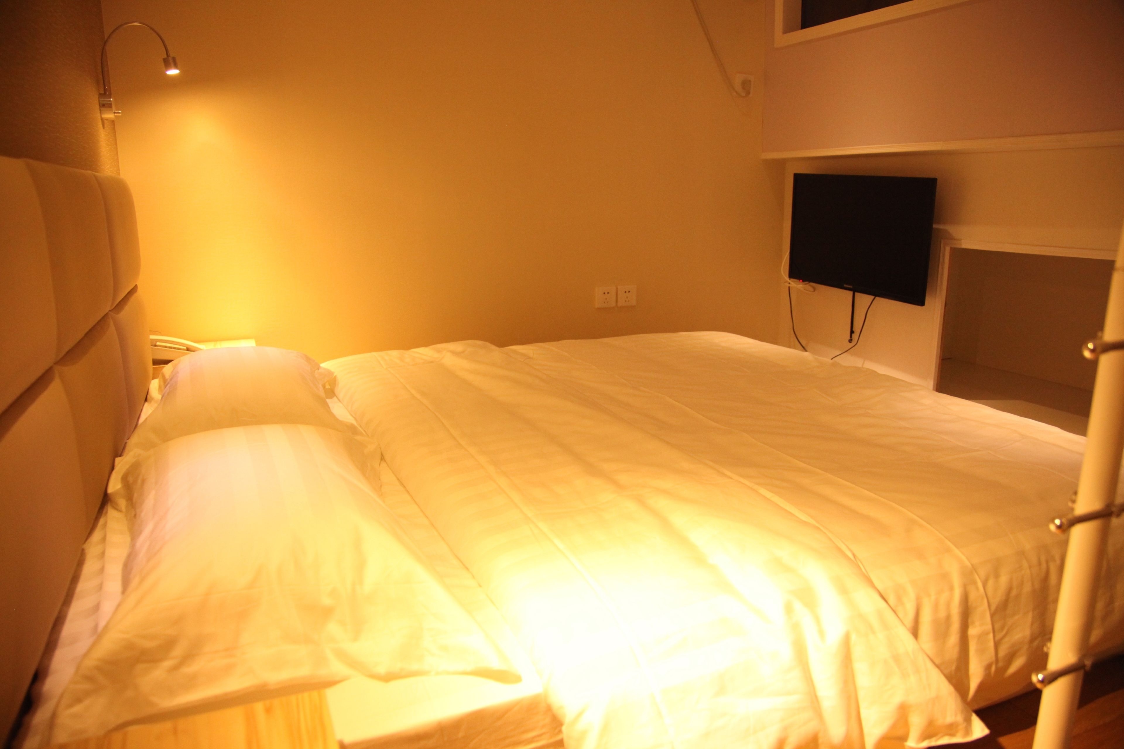 A single bed with white bedding in a room with a sloped ceiling and a mounted TV.