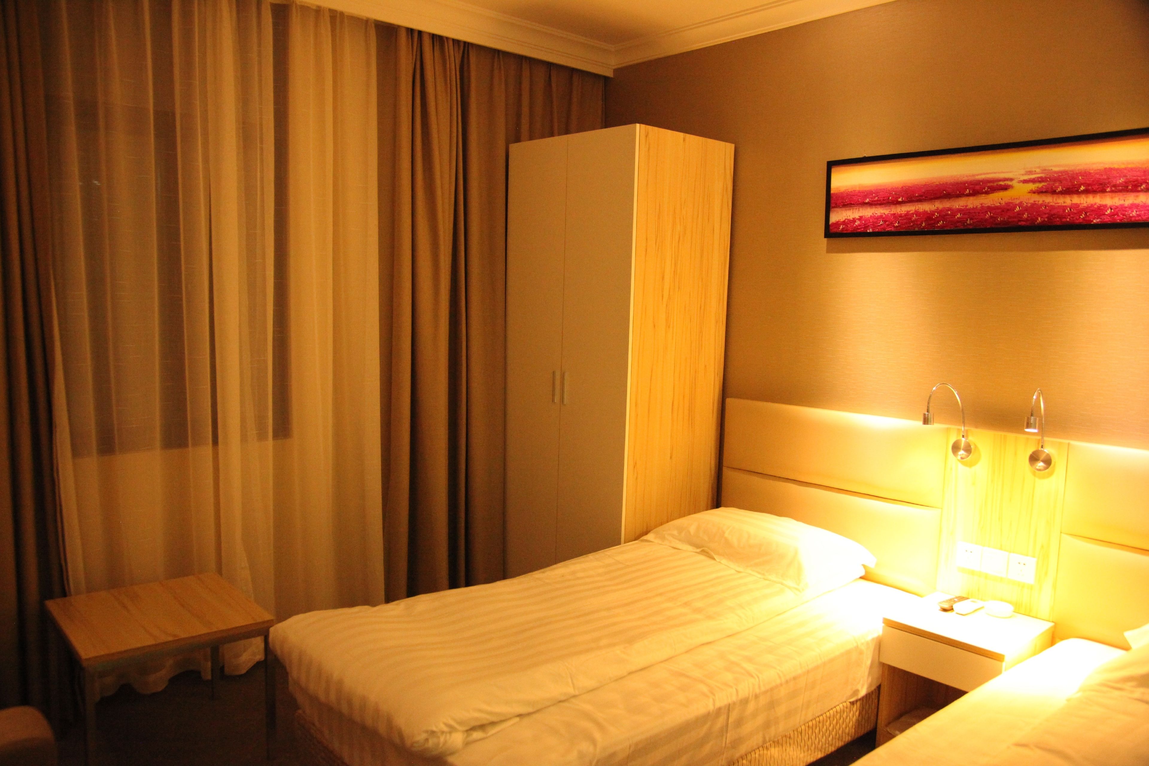 Ett hotellrum med en säng, ett sängbord, en lampa, en garderob och gardiner.