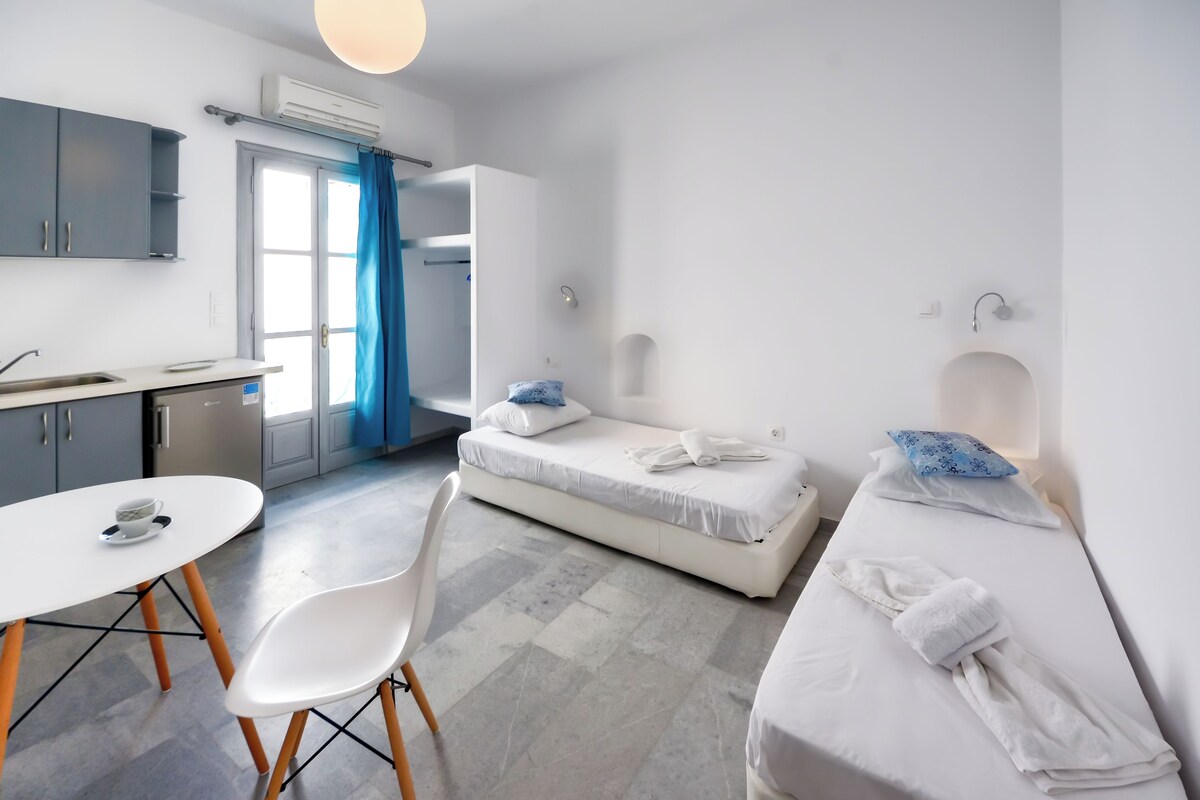 A modern hotel room with a kitchenette, a dining table, and two beds.