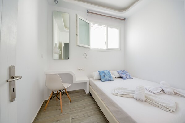 Un dormitorio con cama, una silla, un escritorio, un espejo y una ventana.