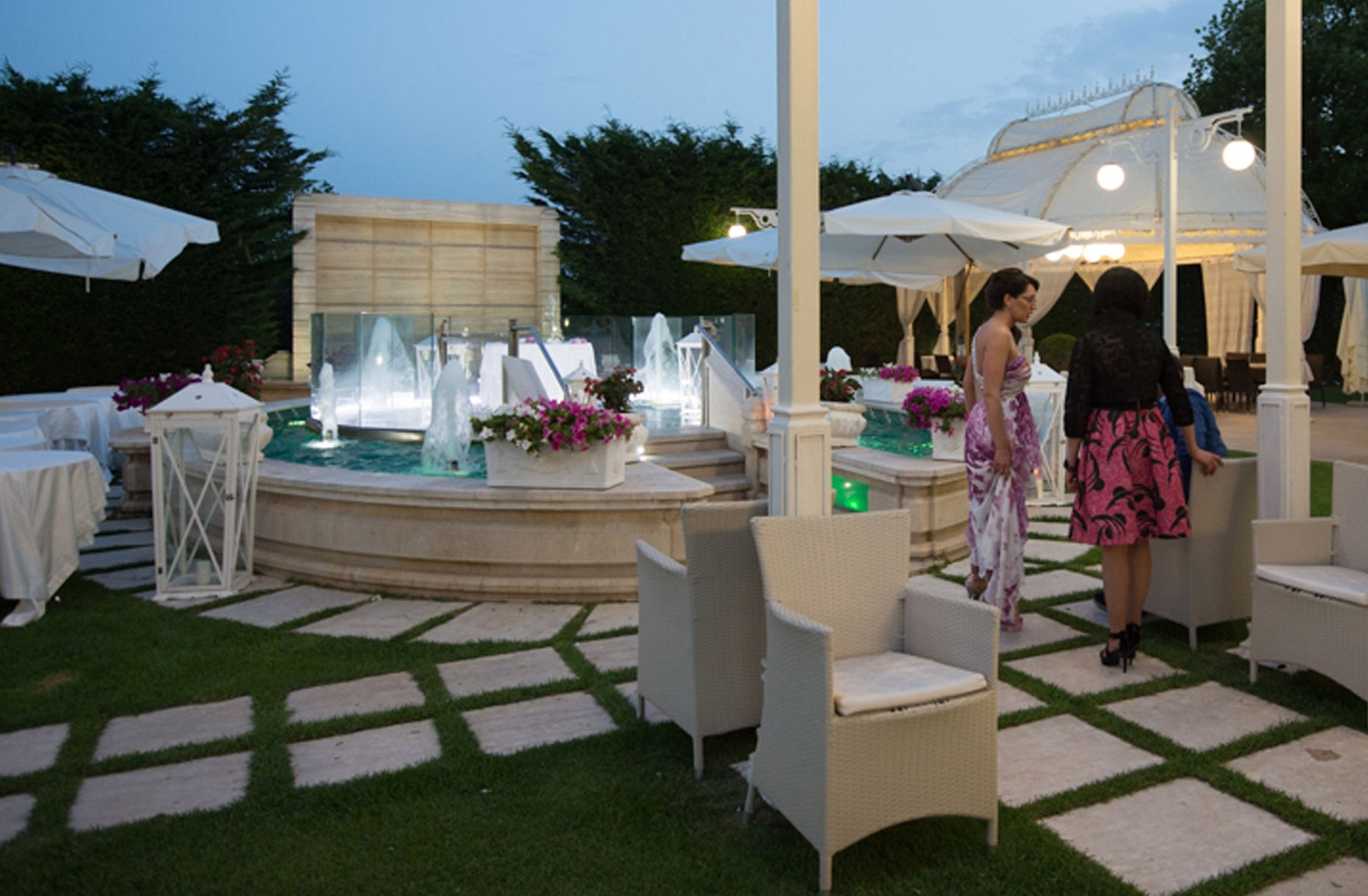An outdoor patio area with a fountain, white outdoor furniture, and a covered seating area.