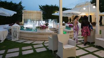 An outdoor patio area with a fountain, white outdoor furniture, and a covered seating area.