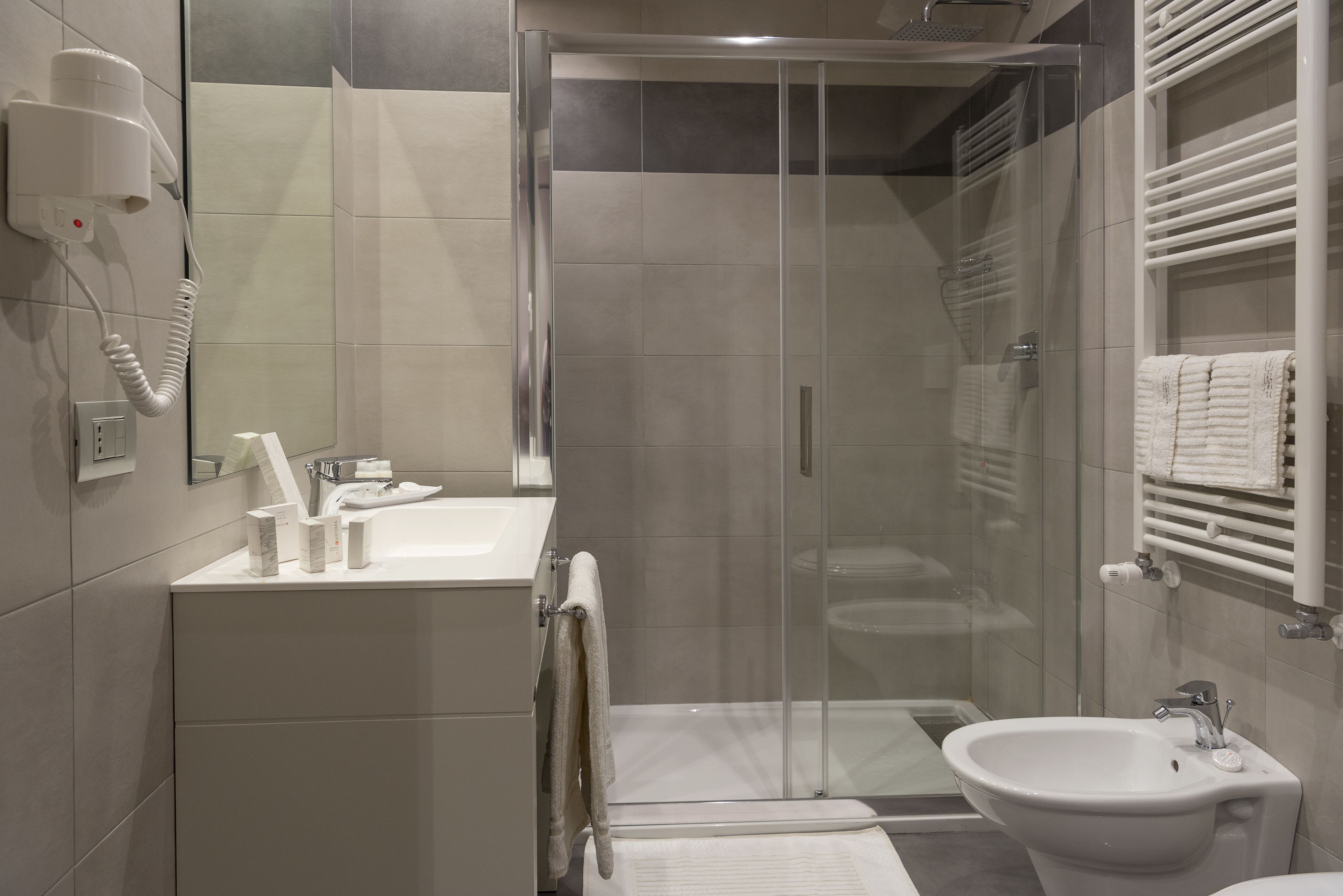 A modern bathroom with a glass-enclosed shower, a sink, and a hairdryer mounted on the wall.
