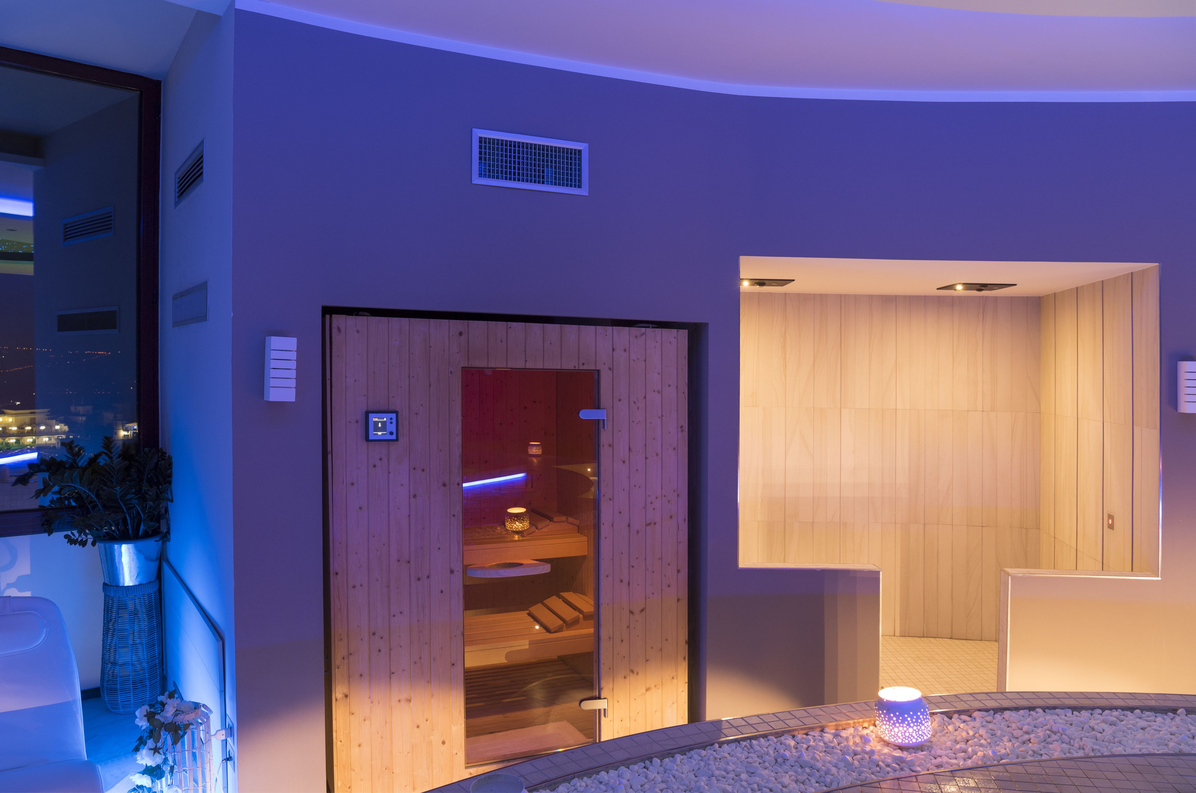 A modern spa room with wooden paneling, a sauna, and a small seating area with a plant.