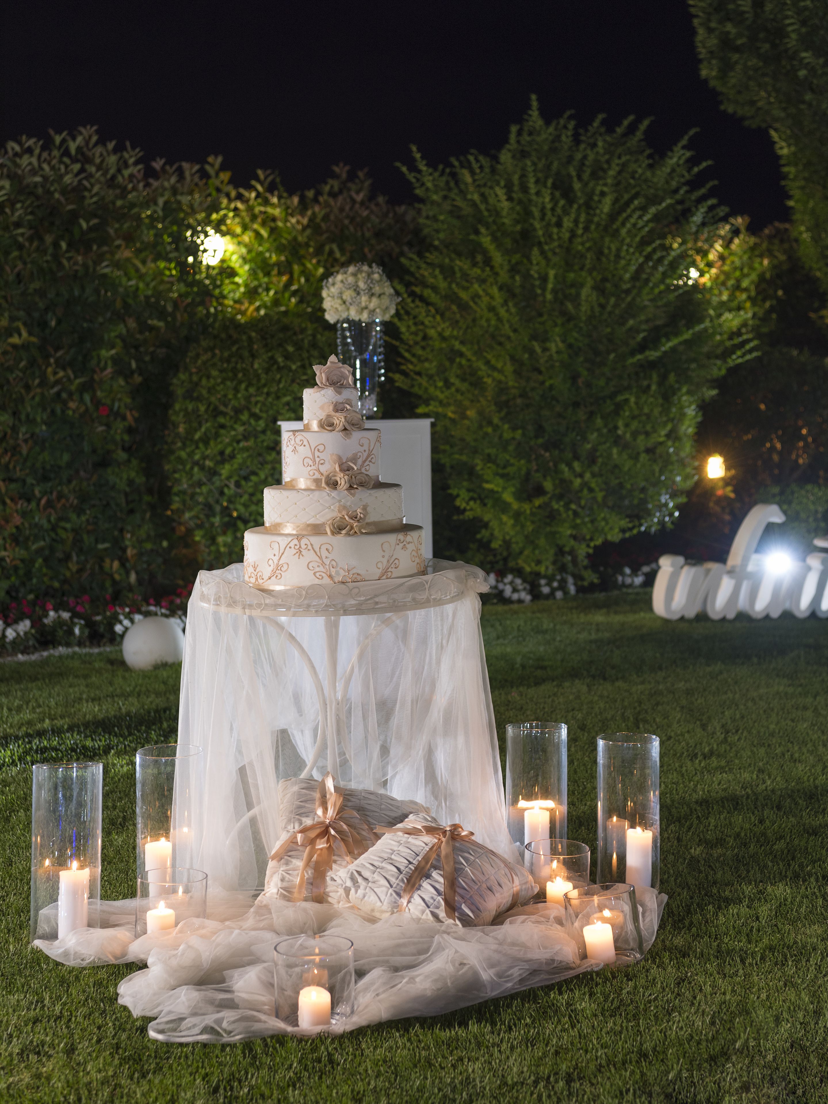A tiered wedding cake on a white tablecloth with candles and glassware.
