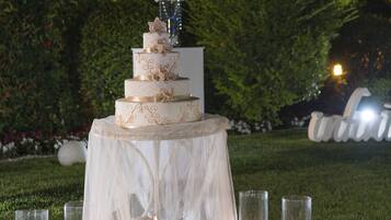 A tiered wedding cake on a white tablecloth with candles and glassware.