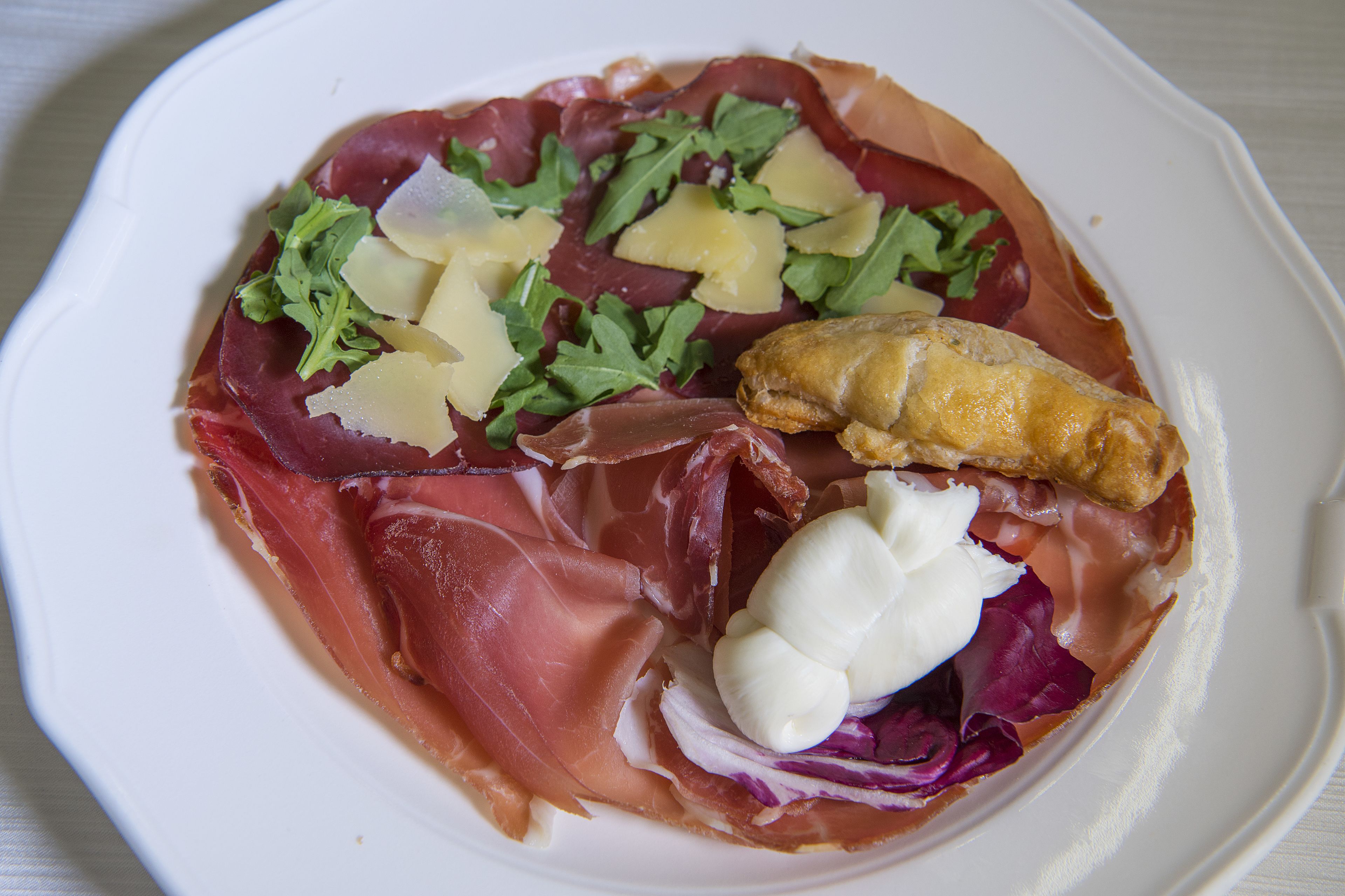 A plate of food with prosciutto, cheese, and greens.