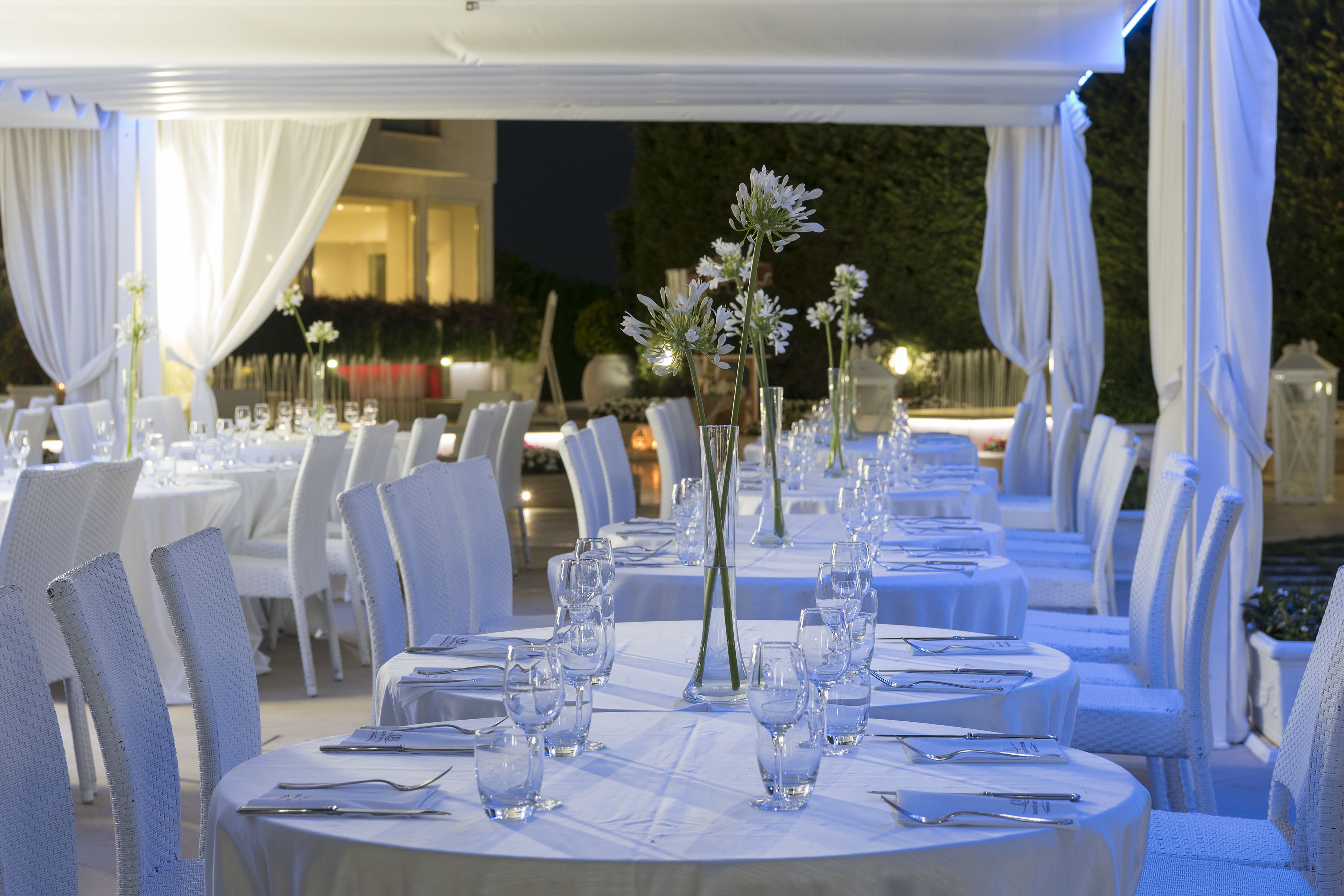 Un espace de restauration en plein air avec des tables rondes dressées pour un événement formel, agrémenté de nappes blanches et de verres élégants.